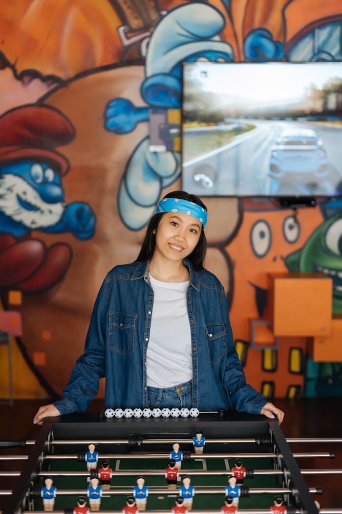 Cheerful woman with headband enjoying a game of foosball in colorful indoor setting.