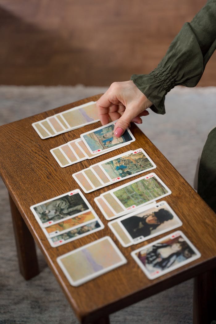 A hand playing solitaire with decorative, unrecognizable cards on a wooden table.